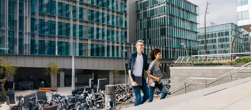 Two professionals with folders walking up the steps of a modern campus building